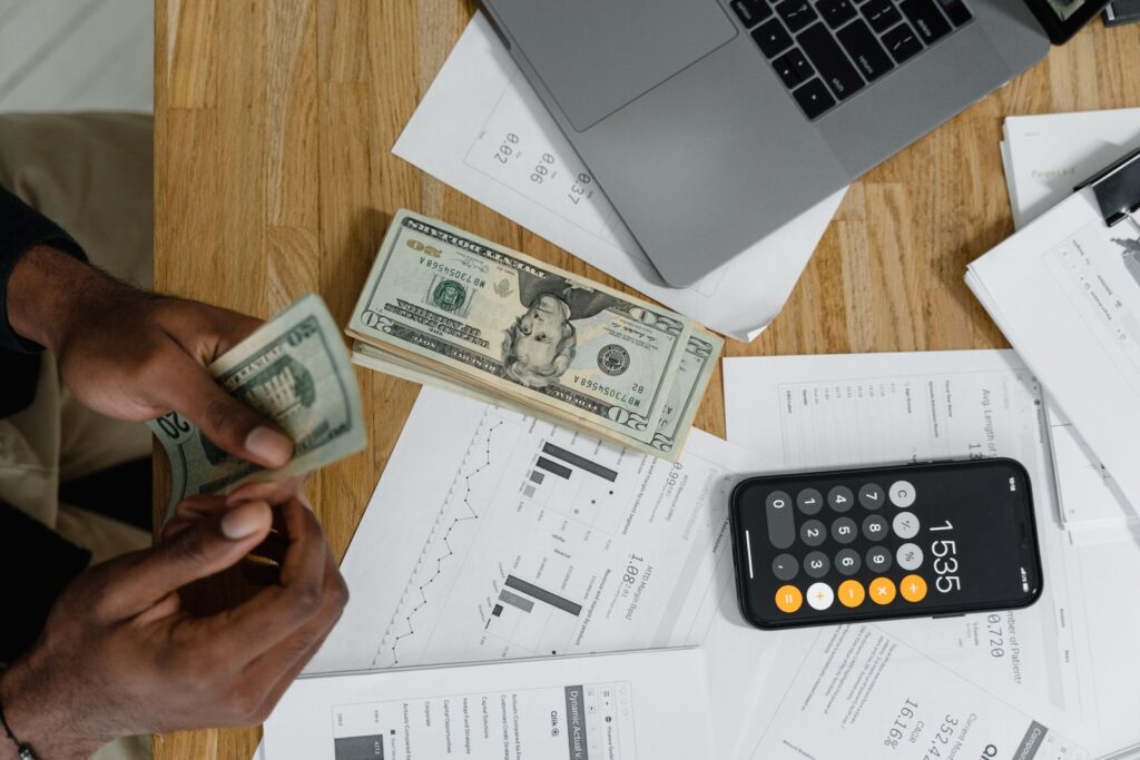 Mãos contando notas de dinheiro ao lado de calculadora e contas a pagar